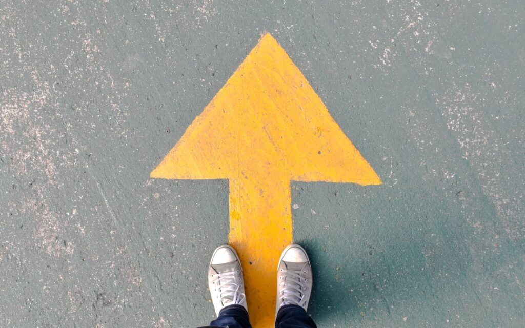 Top view of shoes standing on asphalt with a yellow directional arrow.